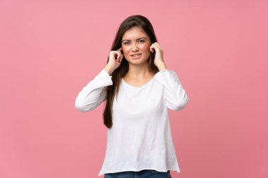 Soyutlanmış pembe arka planı olan genç bir kadın hayal kırıklığına uğramış ve kulaklarını kapatmış.