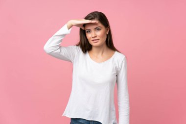 Soyutlanmış pembe arka planı olan genç bir kadın bir şeye bakmak için çok uzaklara bakıyor.