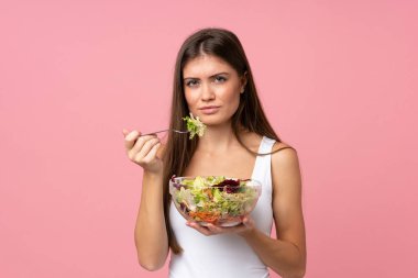 Soyutlanmış pembe duvarda salatalı genç bir kadın.
