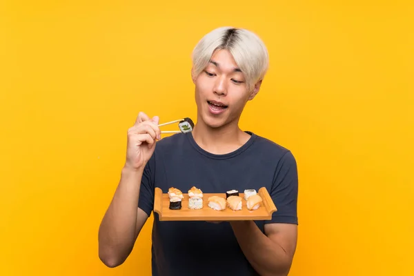 Joven asiático hombre con sushi sobre aislado amarillo fondo — Foto de Stock