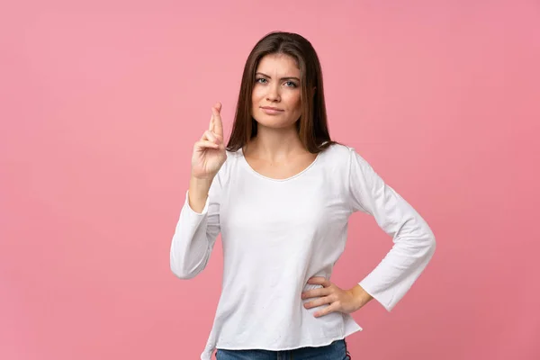 Young woman over isolated pink background with fingers crossing and wishing the best