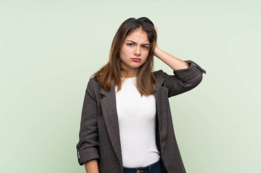 Spor ceketli genç esmer kız izole edilmiş yeşil arka planda hayal kırıklığı ifadesi var ve anlamıyor.