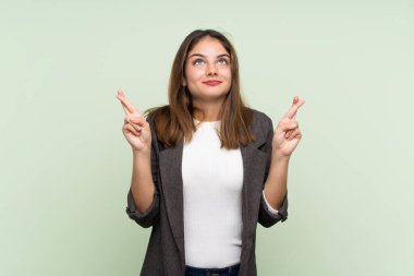 Siyah ceketli genç esmer kız izole edilmiş yeşil arka planda şans diliyor ve en iyisini diliyor.