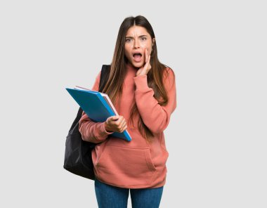 Elinde sürpriz ve şok olmuş yüz ifadesiyle izole edilmiş gri arka plan üzerinde not defterleri tutan genç öğrenci kadın.