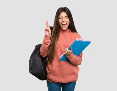 İzole edilmiş gri arka plan üzerinde parmakları çapraz olan not defterleri tutan genç öğrenci kadın.