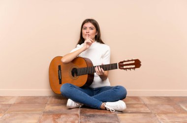 Gitarlı genç bir kadın yerde sessizce oturuyor.