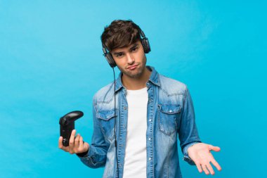 Soyutlanmış mavi arka planda video oyunlarında oynayan yakışıklı bir genç.