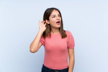 Genç esmer kız izole edilmiş mavi arka planda bir şeyler dinliyor.