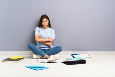 Yerde bir sürü kitabı olan ve kollarını kavuşturan genç bir bayan öğrenci.