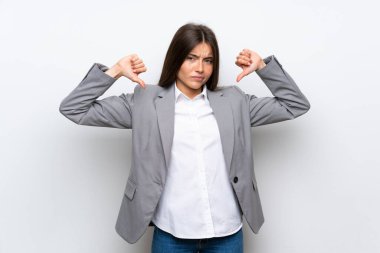 Soyutlanmış beyaz arka planda genç bir iş kadını baş parmağını aşağı gösteriyor.