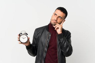 Soyutlanmış beyaz arka planı olan genç bir adam klasik çalar saat tutuyor.