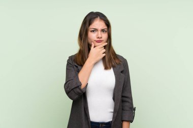 Ceketi olan esmer genç bir kız izole edilmiş yeşil arka planı düşünüyor.