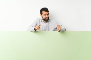 Sakallı, kocaman yeşil bir afiş tutan yakışıklı genç adam para hareketi yapıyor.