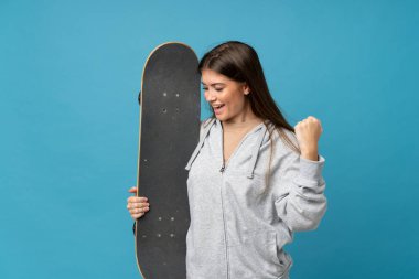 Genç bir kadın mavi arka planda paten kayıyor ve zafer jestleri yapıyor.