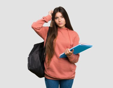 Elinde hüsran ifadesi olan not defterleri tutan ve izole edilmiş gri arkaplanı anlamayan genç bir öğrenci kadın.