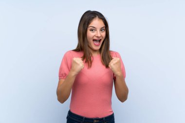 Genç esmer kız izole edilmiş mavi arka planda zaferi kutluyor.