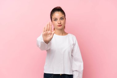 Soyutlanmış pembe arka planda genç esmer kız dur hareketi yapıyor.