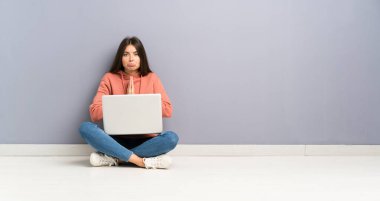 Dizüstü bilgisayarlı genç bir kız yerde yalvarıyor.