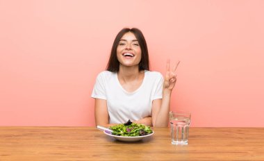 Salatalı genç bir kadın gülümsüyor ve zafer işareti gösteriyor.