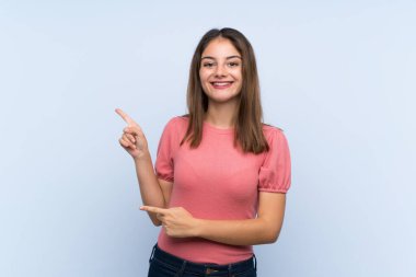 Genç esmer kız izole edilmiş mavi arka planda parmağını yana doğru gösteriyor.