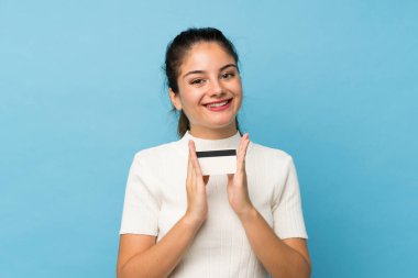 Genç esmer kız izole edilmiş mavi arka planda elinde bir kredi kartıyla