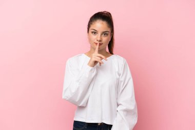 Soyutlanmış pembe arka planda genç bir esmer kız sessizlik işareti gösteriyor. Parmağını ağzına sok.