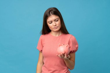 Soyutlanmış mavi arka planı olan genç bir kadın büyük bir kumbara tutuyor.