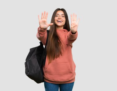 Elinde not defterleri olan genç bir bayan parmak sayıyor. Gri arka planda.