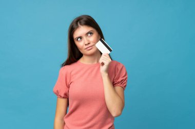 Soyutlanmış mavi arka planı olan genç bir kadın kredi kartı tutuyor.