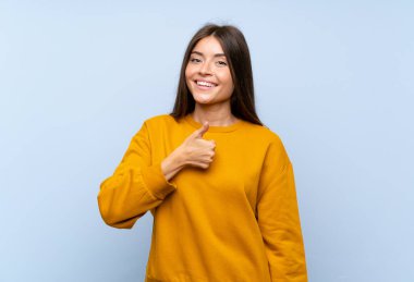 Kafkas asıllı genç bir kadın mavi duvardan izole edilmiş bir şekilde baş parmak işareti yapıyor.