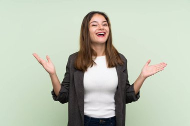 Siyah ceketli genç esmer kız izole edilmiş yeşil arka planda gülümsüyor.