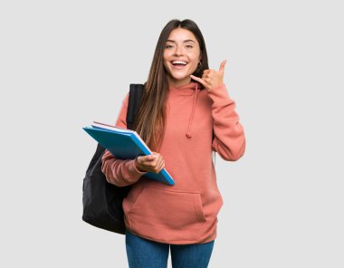 Elinde not defterleri olan genç bir bayan telefon hareketi yapıyor. Gri arka planda beni ara.