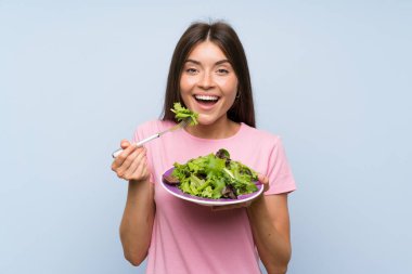 Izole mavi arka plan üzerinde salata ile genç kadın