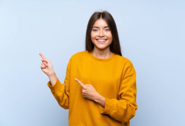 Izole mavi duvar üzerinde beyaz genç kadın yan parmak işaret