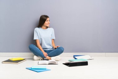 Yerde bir sürü kitabı olan genç bir bayan öğrenci yan tarafa bakıyor.