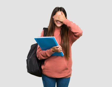 Elinde not defterleri tutan genç bir bayan. Gri arka planda, elleri ve gözleri kapalı.