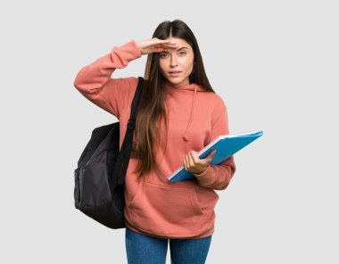 Elinde defterler olan genç bir bayan izole edilmiş gri bir arkaplanı incelemek için elleriyle uzaklara bakıyor.