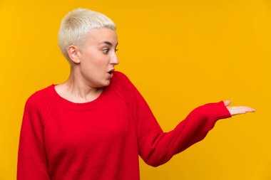 Sarı duvarın üzerinde beyaz kısa saçlı genç bir kız. Palmiyesinde hayali bir yer tutuyor.