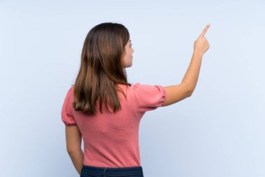 İzole edilmiş mavi arka planda genç esmer kız işaret parmağıyla işaret ediyor.