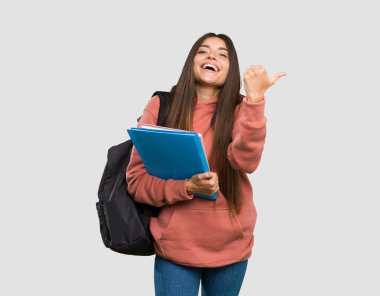 Elinde notlar tutan genç bir bayan parmak işareti ve izole edilmiş gri arkaplanda gülümsüyor.