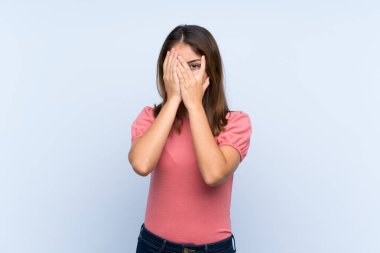 Genç esmer kız izole edilmiş mavi arka planda gözleri kapatıyor ve parmaklarından bakıyor.