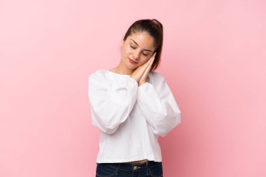 Soyutlanmış pembe arka planda genç bir esmer kız uyku jesti yapıyor.