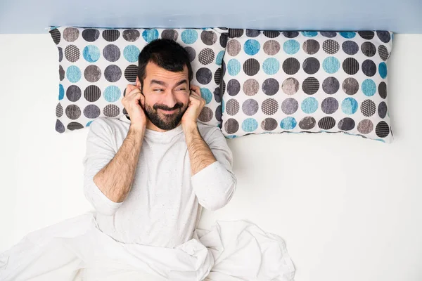 Man in bed in top view frustrated and covering ears