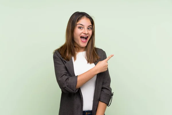 Giovane Ragazza Bruna Con Blazer Sfondo Verde Isolato Sorpreso Indicando — Foto Stock