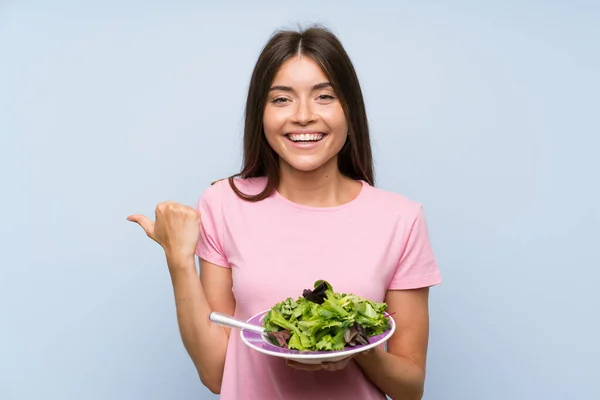 Mujer Joven Con Ensalada Sobre Fondo Azul Aislado Apuntando Hacia — Foto de Stock