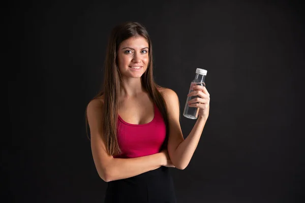 Giovane donna sportiva con una bottiglia d'acqua su sfondo nero isolato — Foto Stock