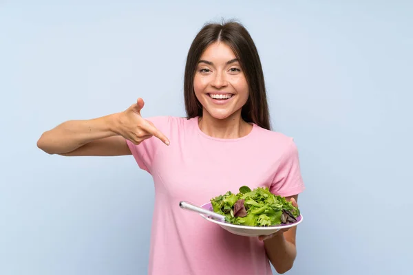 Giovane donna con insalata su sfondo blu isolato — Foto Stock