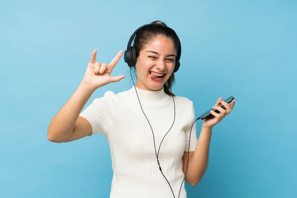 Jovem Morena Sobre Fundo Azul Isolado Usando Celular Com Fones — Fotografia de Stock