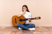 Young woman with guitar sitting on the floor thinking an idea