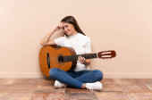 Mladá žena s kytarou sedící na podlaze a smějící se